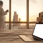 Close-up laptop on bed with man in bathrobe background